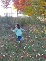 A child running in a teal children's wool cardigan with a crew neck collar, patch pockets, english rib knit stitch body, and a finely detailed raglan sleeve