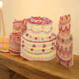 Still life image of a concertina style greeting card made up of four ornately decorated cakes, displayed on a mantel