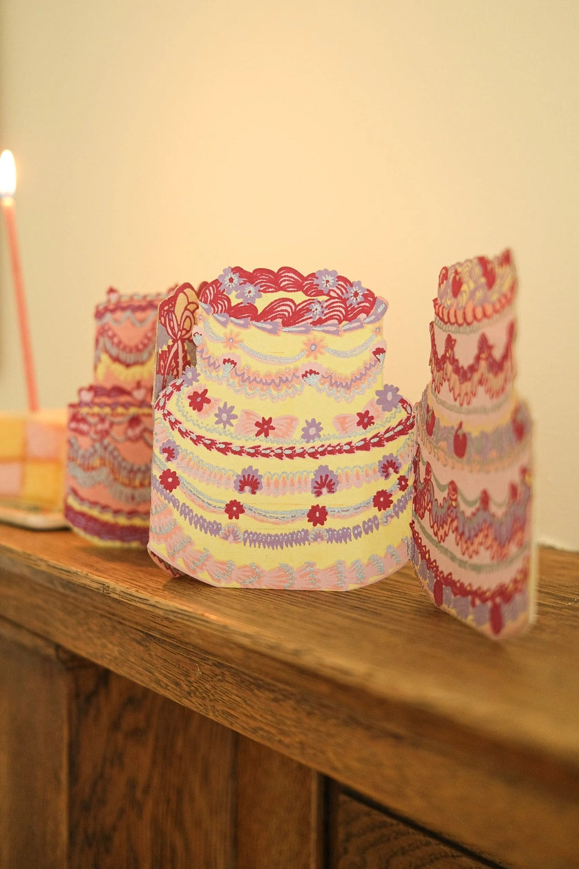 Still life image of a concertina style greeting card made up of four ornately decorated cakes, displayed on a mantel