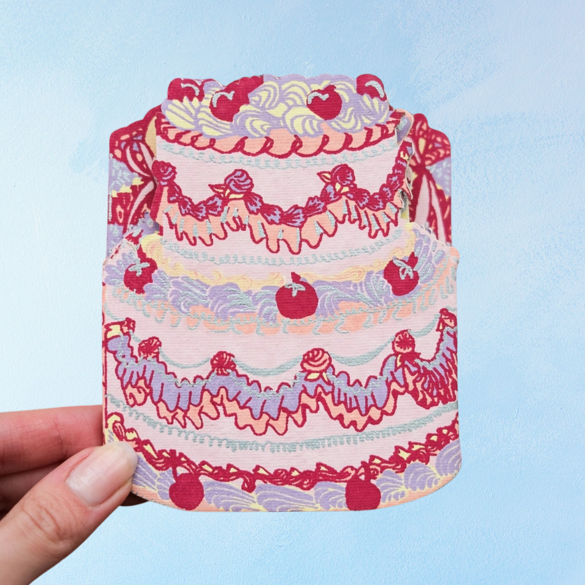 Birthday cake concertina card by East End Press showing one of the individual cakes. The cake is decorated with various piping tips, cherries, and features colours of purple, red, yellow, and pink