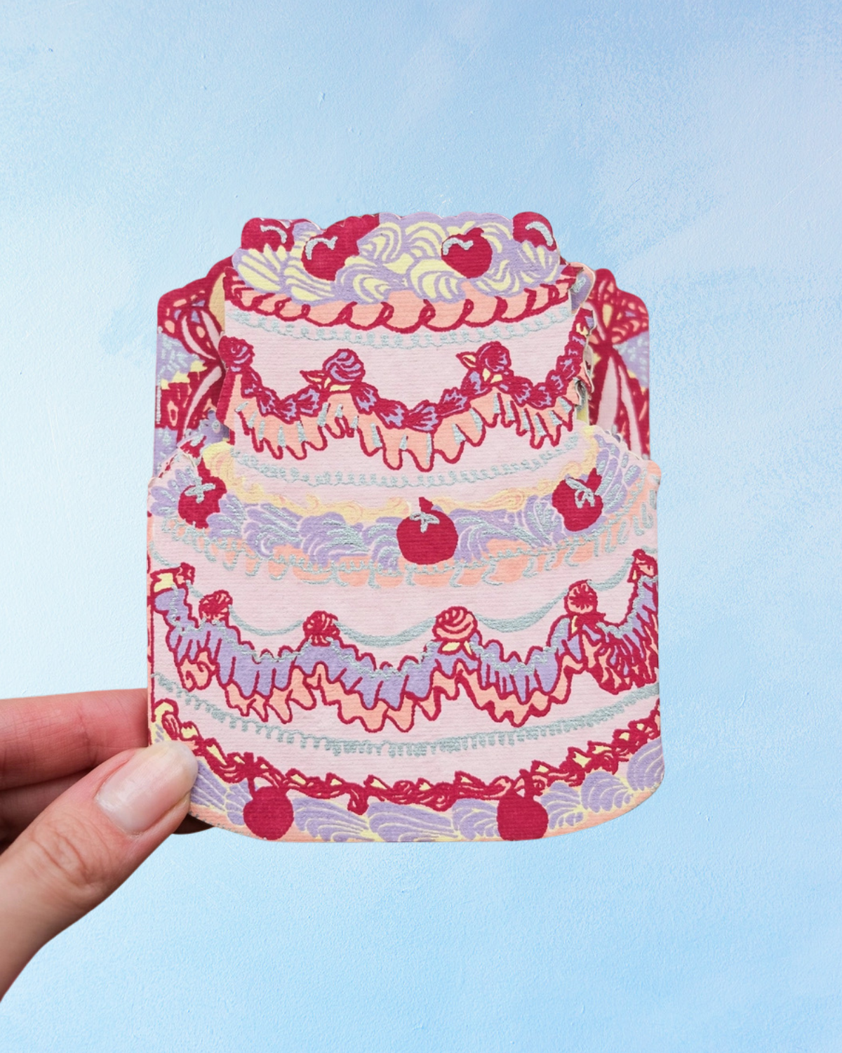Birthday cake concertina card by East End Press showing one of the individual cakes. The cake is decorated with various piping tips, cherries, and features colours of purple, red, yellow, and pink