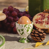 ceramic egg cup with a white base and moss toned green splatter design, photographed in a still life with an egg inside 