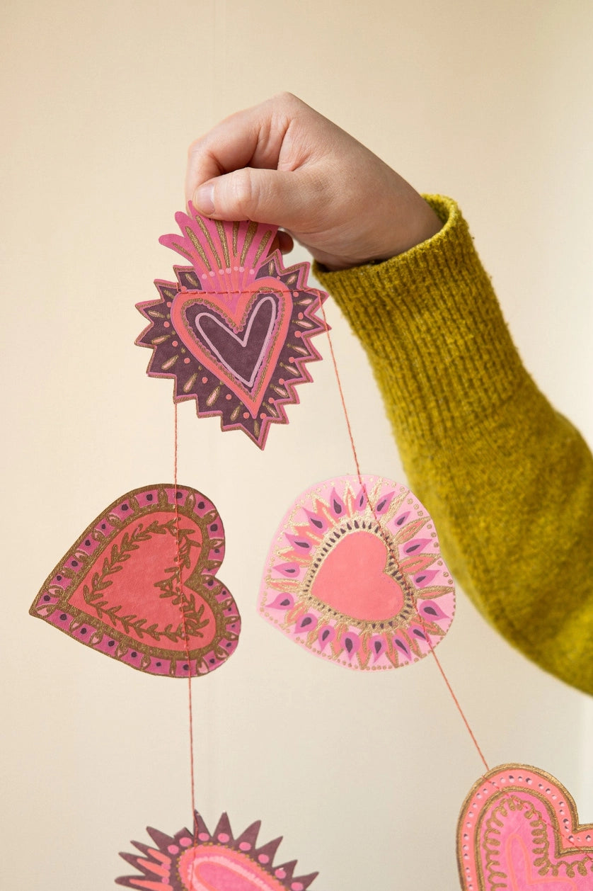 Hand holding a string with heart-shaped decorations against a beige background