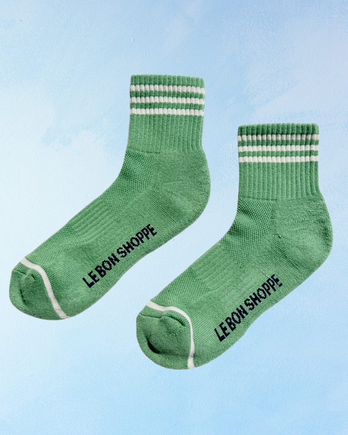 Green socks with white stripes and 'LE Bon Shoppe' branding on a light blue background