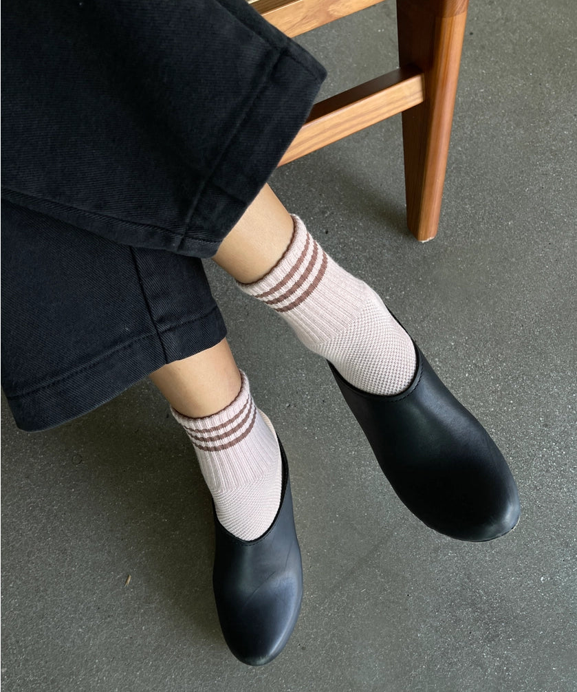 Person wearing black shoes and light pink socks with brown stripes, sitting on a wooden chair.