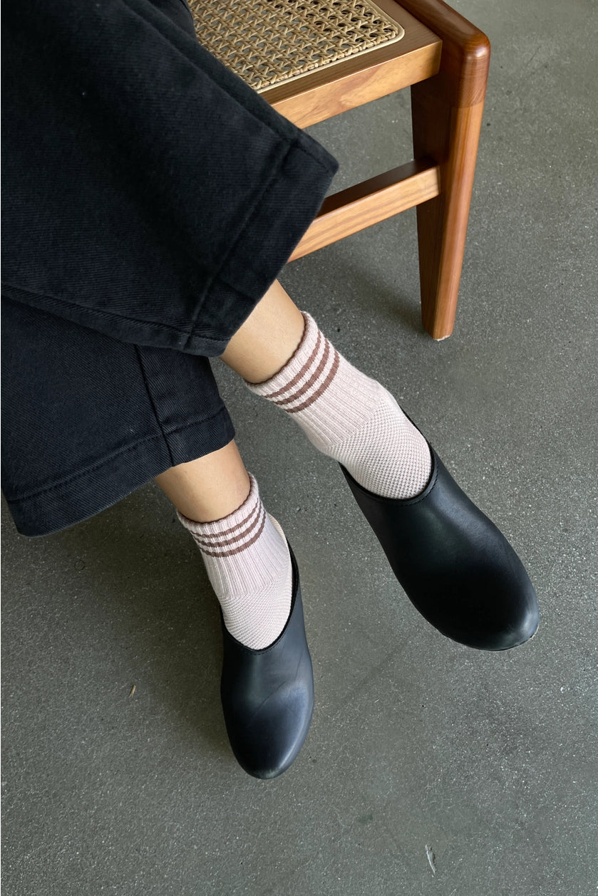 Person wearing black shoes and light pink socks with brown stripes, sitting on a wooden chair.