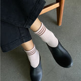 Person wearing black shoes and light pink socks with brown stripes, sitting on a wooden chair.