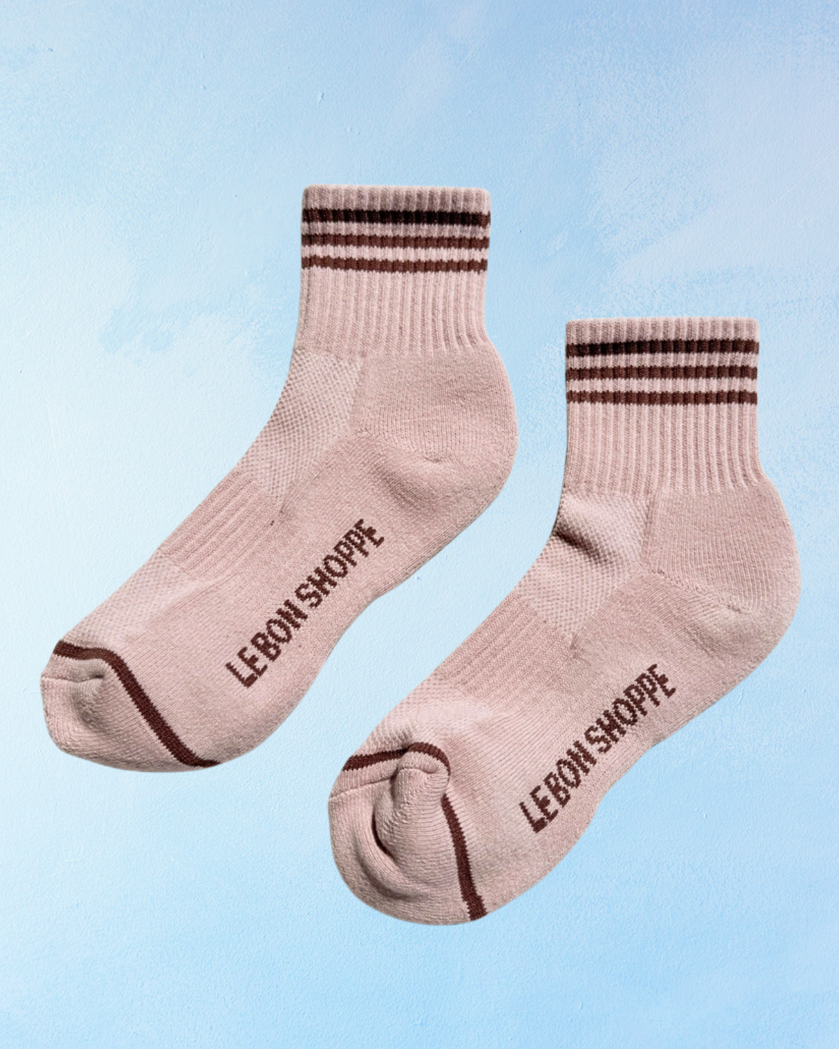 Pair of pink socks with brown stripes and 'LEBON SHOPPE' branding on a light blue background