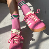 Pink sneakers with white laces and green striped socks on a light gray surface.