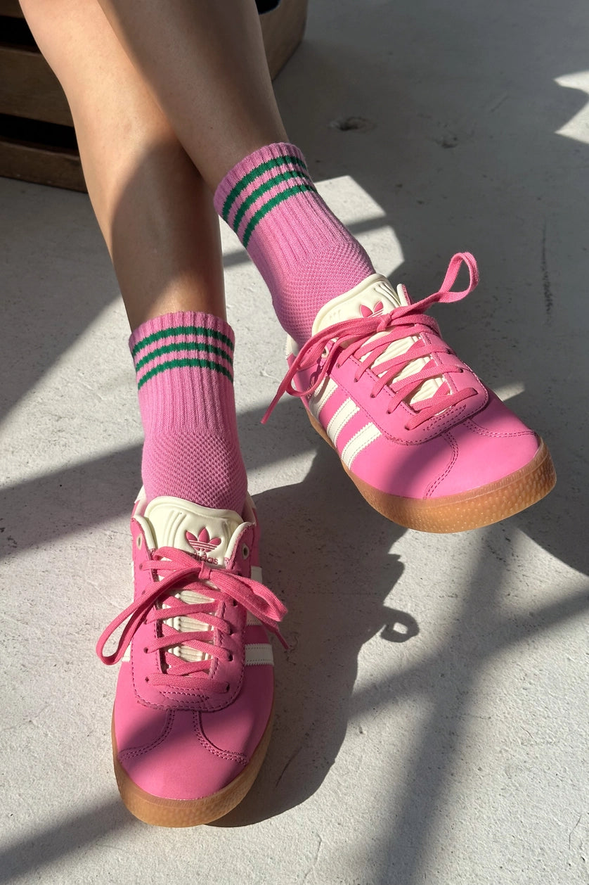 Pink sneakers with white laces and green striped socks on a light gray surface.