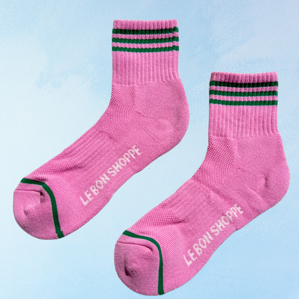 Pink socks with green stripes and 'LE BON SHOPPE' branding on a light blue background