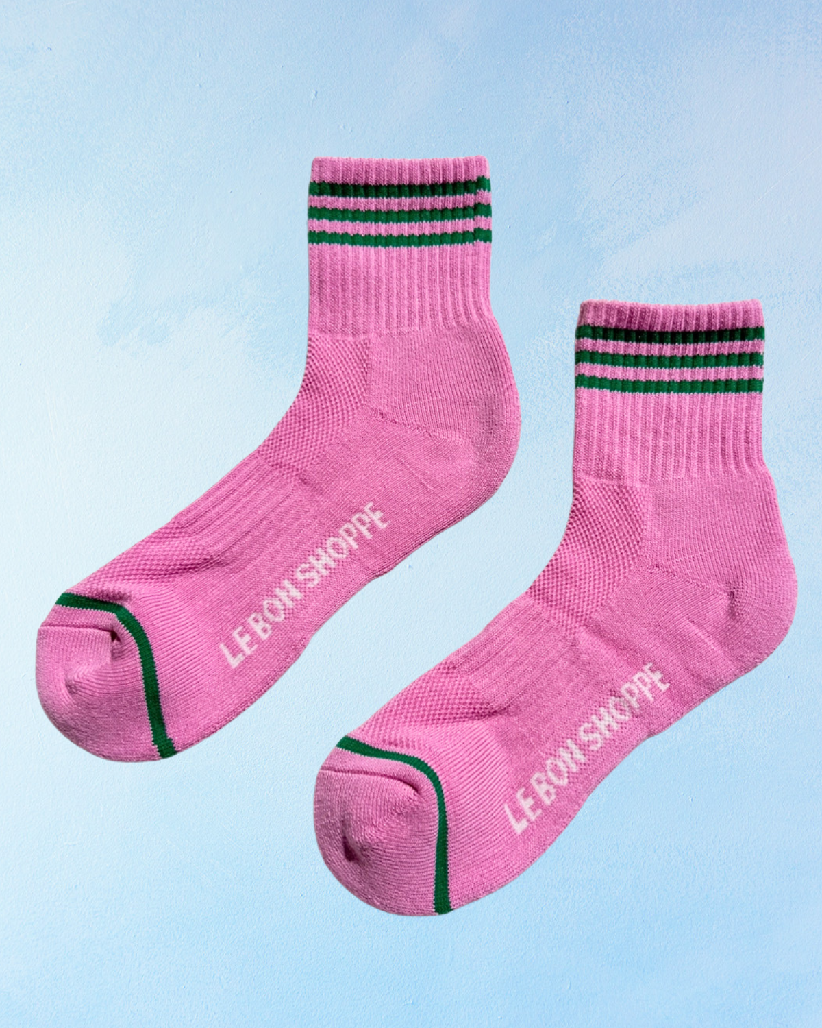 Pink socks with green stripes and 'LE BON SHOPPE' branding on a light blue background