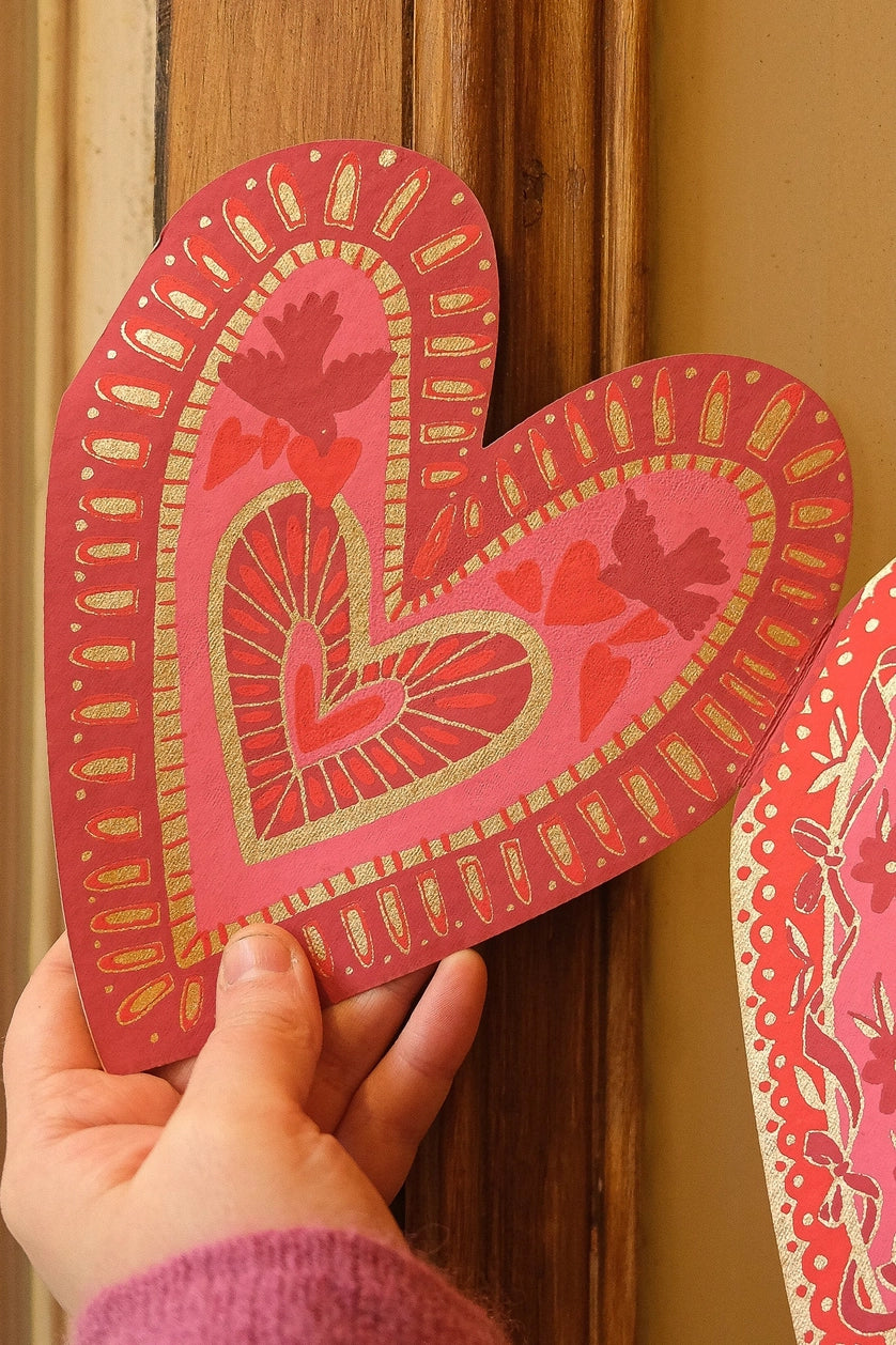 Paper heart with screen printed details like lines, birds, and additional hearts in pink and red with metallic gold