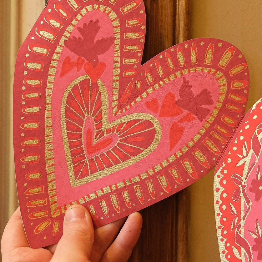 Paper heart with screen printed details like lines, birds, and additional hearts in pink and red with metallic gold