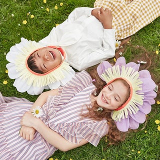 Two children lying in grass with flower paper bonnets on