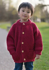 Little boy in a children's wool cardigan with a crew neck collar, patch pockets, english rib knit stitch body, and a finely detailed raglan sleeve.