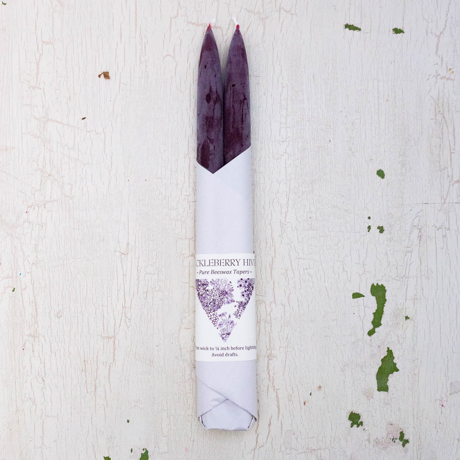 Set of two beeswax tapers in a deep burgundy colour, bottom half wrapped in white paper by Huckleberry Hives.