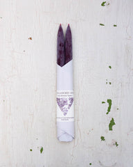 Set of two beeswax tapers in a deep burgundy colour, bottom half wrapped in white paper by Huckleberry Hives.