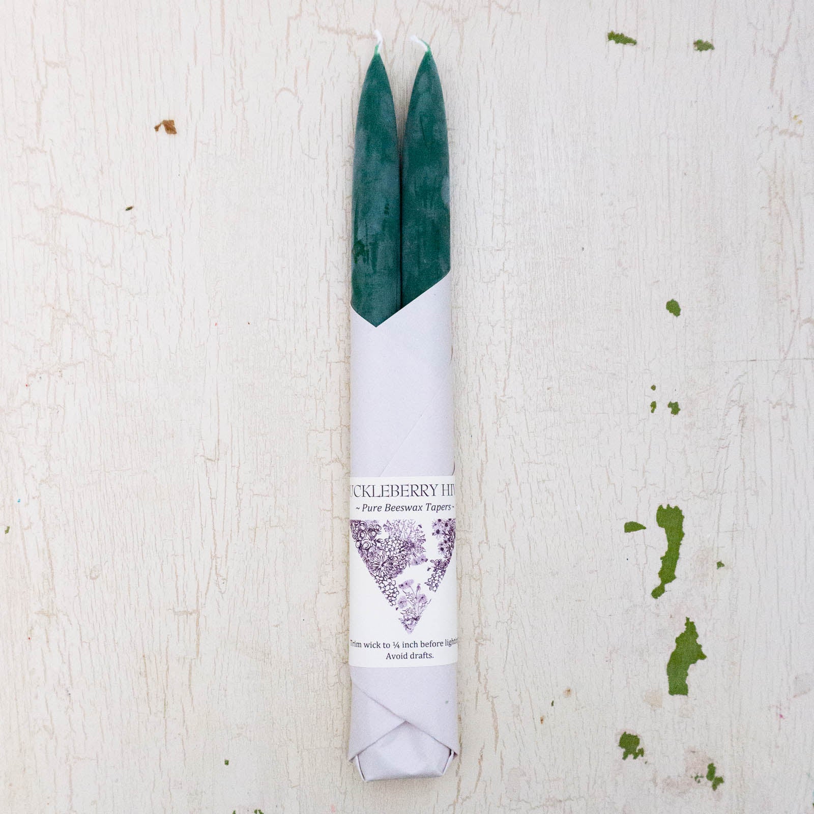 Set of two beeswax tapers in a dark green colour, bottom half wrapped in white paper by Huckleberry Hives.