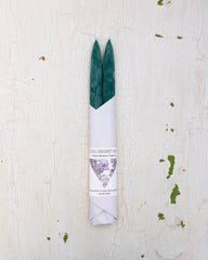 Set of two beeswax tapers in a dark green colour, bottom half wrapped in white paper by Huckleberry Hives.