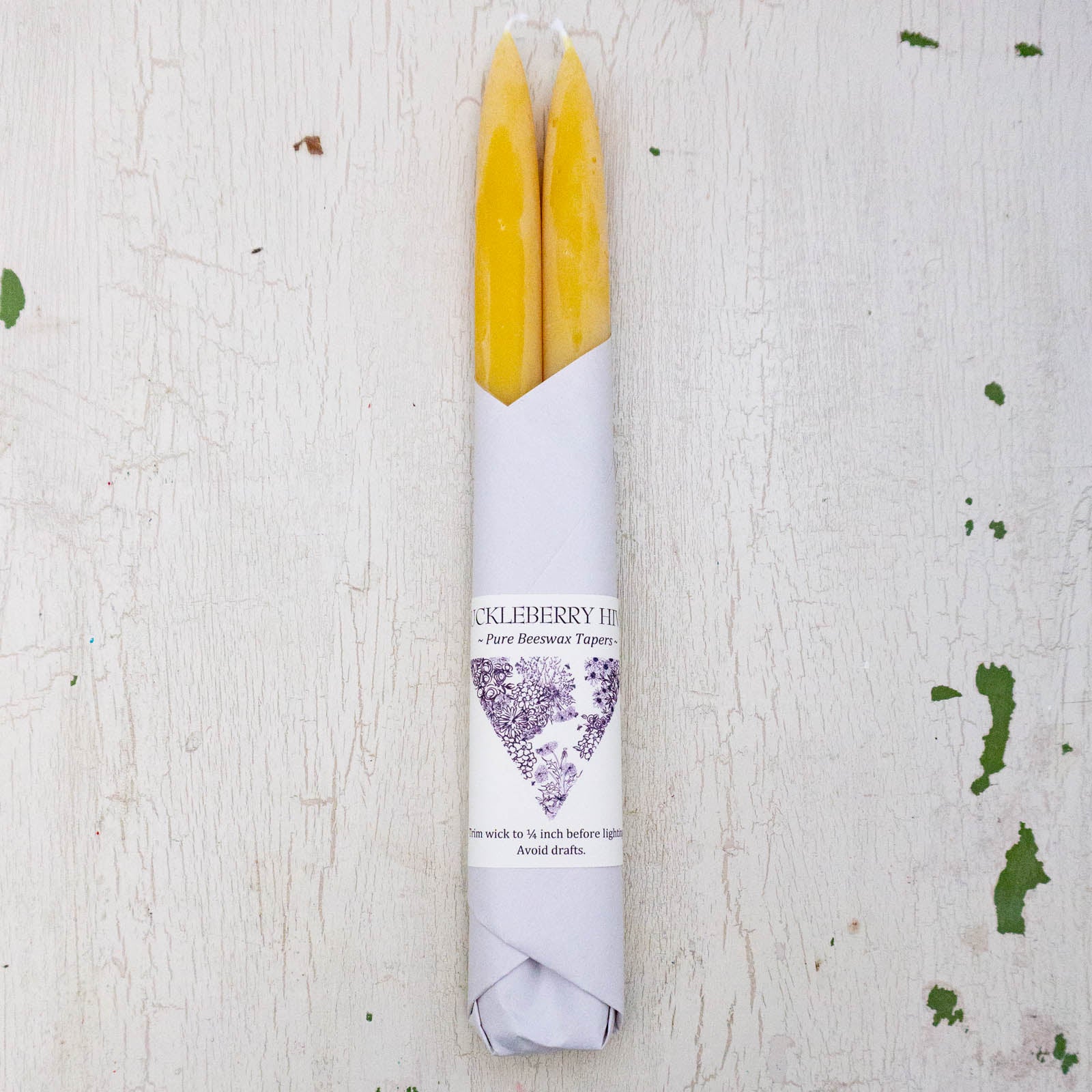 Set of two beeswax tapers in traditional yellow colour, bottom half wrapped in white paper by Huckleberry Hives.