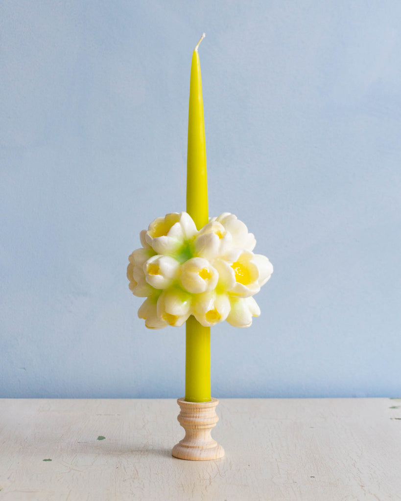 A yellow taper candle with a large white and yellow flower candle slid halfway down the taper