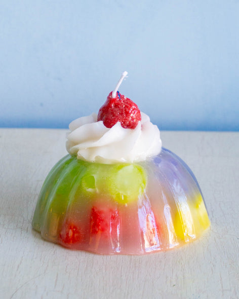 A candle in the shape of a fruity aspic with cream on top 