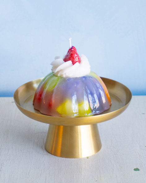 A candle in the shape of a fruity aspic with cream on top 