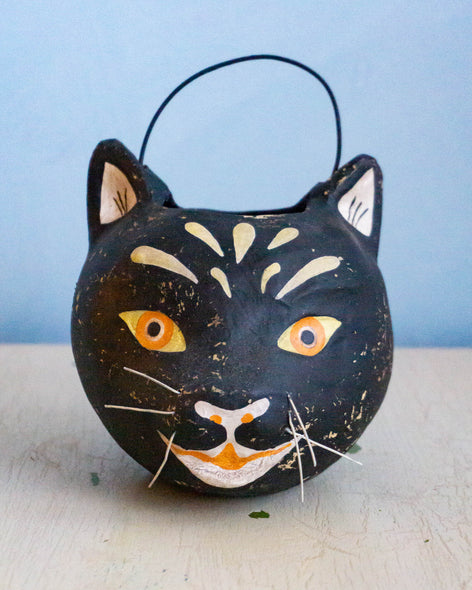 A black basket in the shape of a cat's head. Painted with the details of the face and adorned with little whiskers.