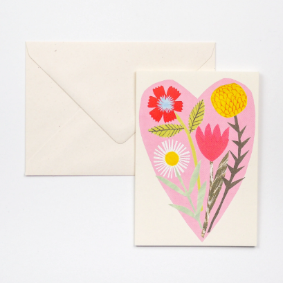 A greeting card featuring beautiful bouquet of flowers layered on a soft pink heart.