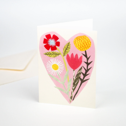 A greeting card featuring beautiful bouquet of flowers layered on a soft pink heart.