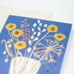 A greeting card featuring a glass vase with a posy of grasses, seed heads and simple, humble flowers.
