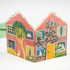 A greeting card featuring a double sided collage of a sweet red-brick house with a kissing couple in one window and a happy cat in another.