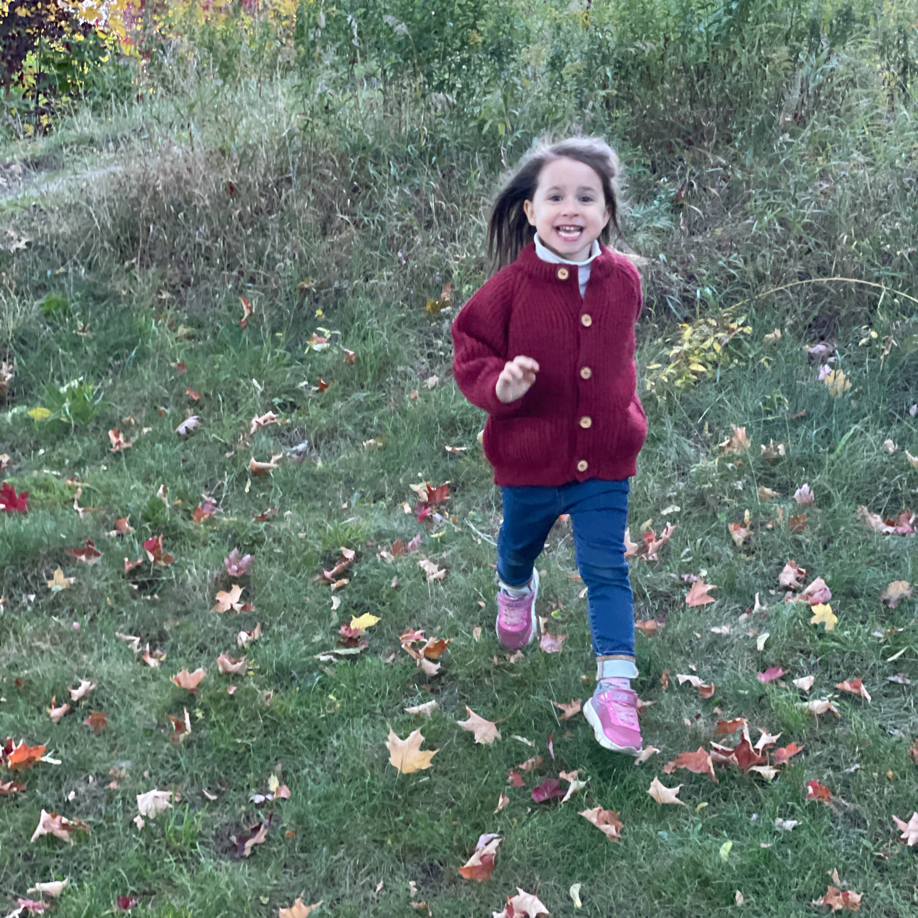 A child running in a children's wool cardigan with a crew neck collar, patch pockets, english rib knit stitch body, and a finely detailed raglan sleeve