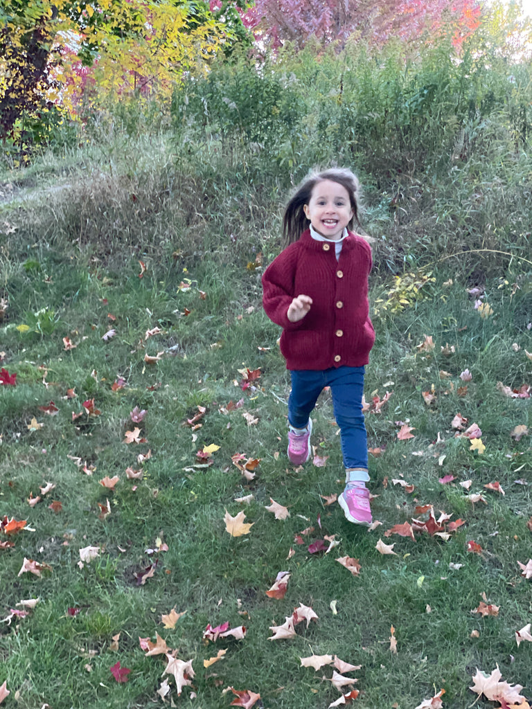 A child running in a children's wool cardigan with a crew neck collar, patch pockets, english rib knit stitch body, and a finely detailed raglan sleeve