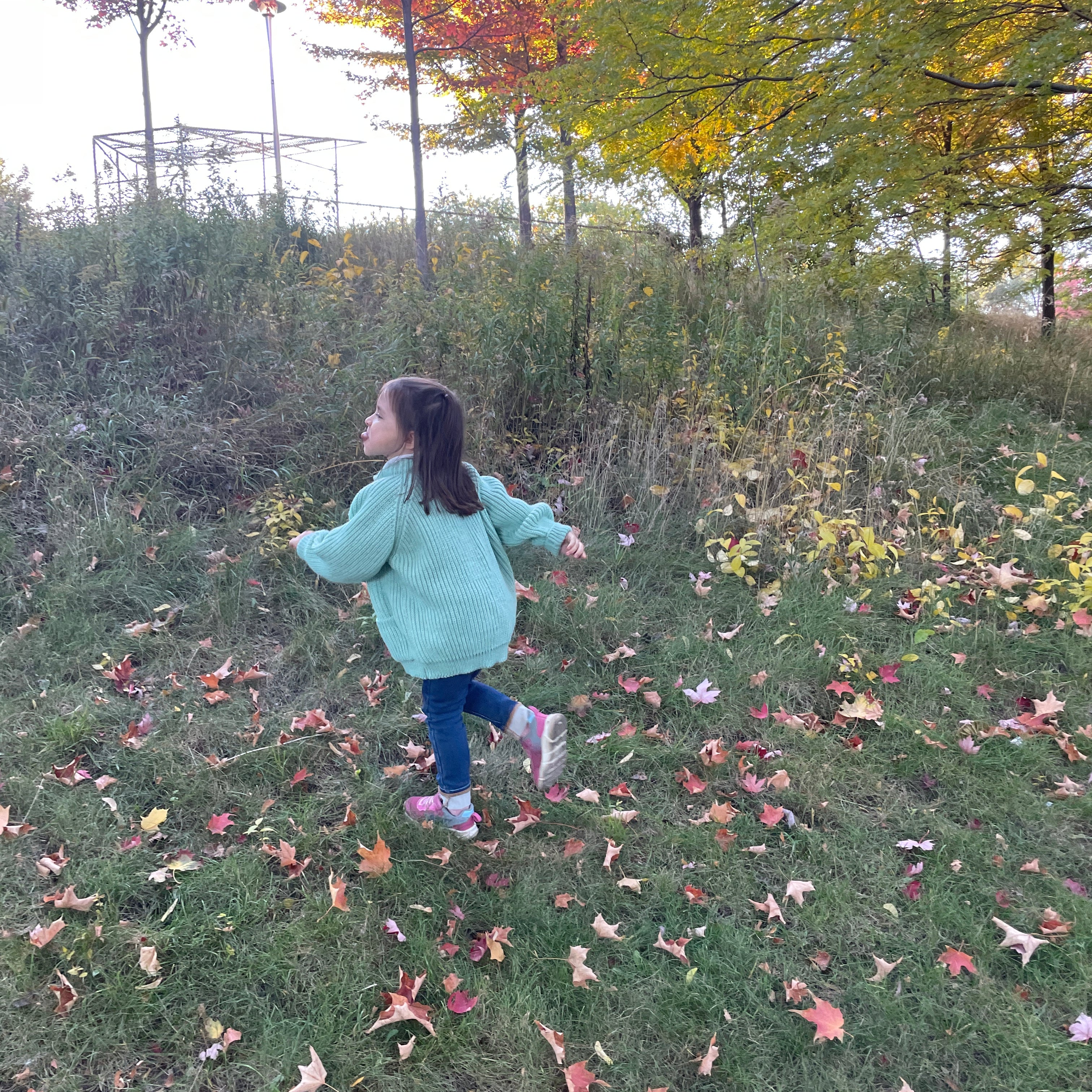 A child running in a teal children's wool cardigan with a crew neck collar, patch pockets, english rib knit stitch body, and a finely detailed raglan sleeve