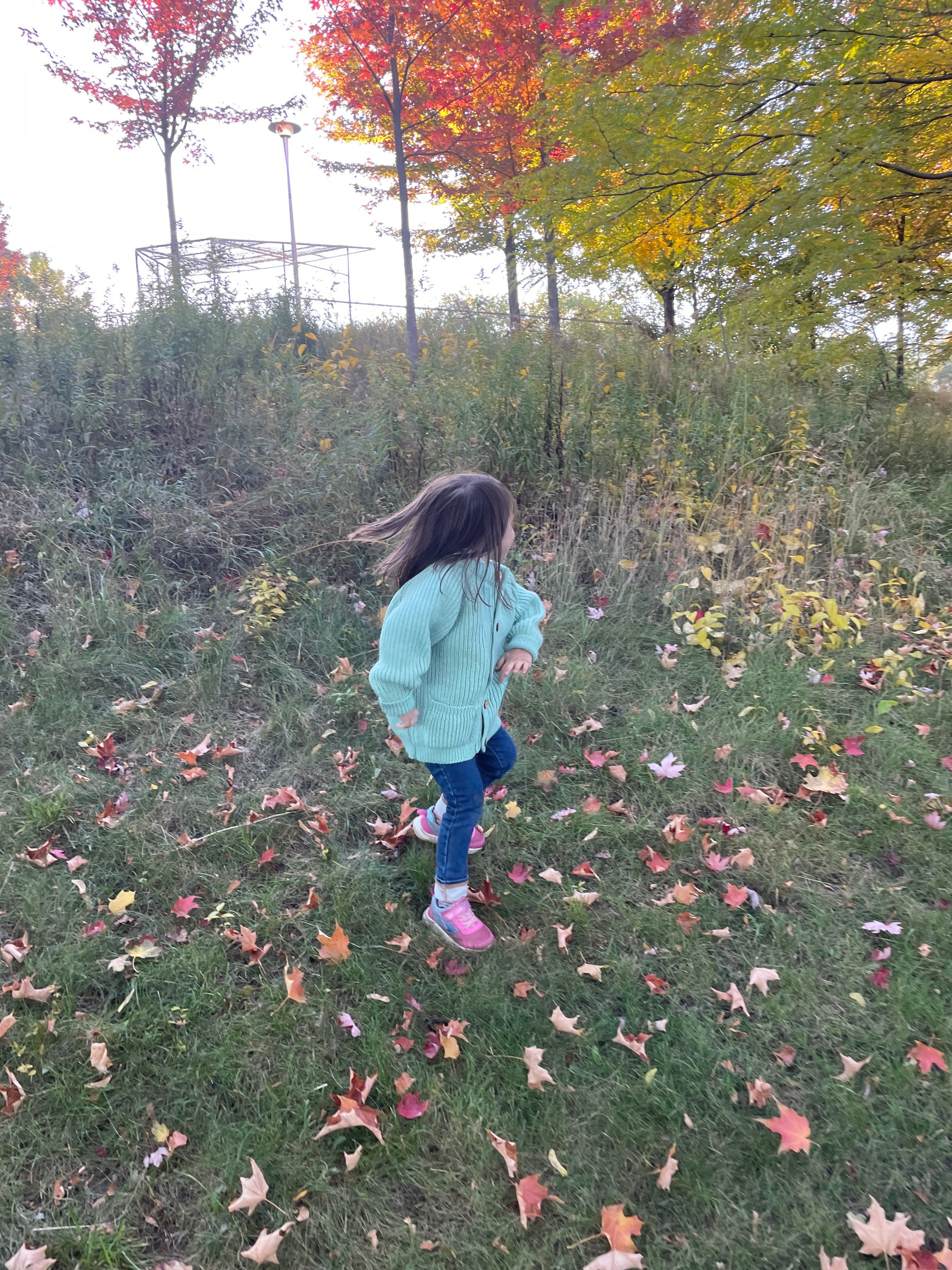A child running in a teal children's wool cardigan with a crew neck collar, patch pockets, english rib knit stitch body, and a finely detailed raglan sleeve