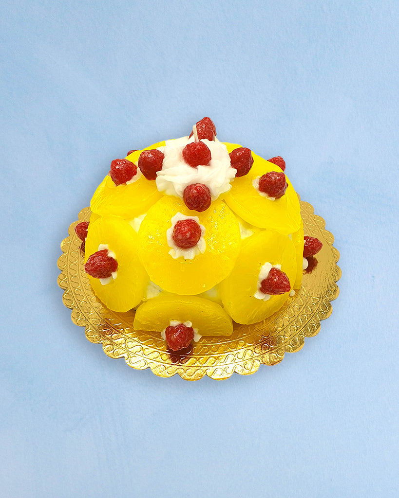a candle shaped like a full-sized pineapple upside down cake w raspberries on it 