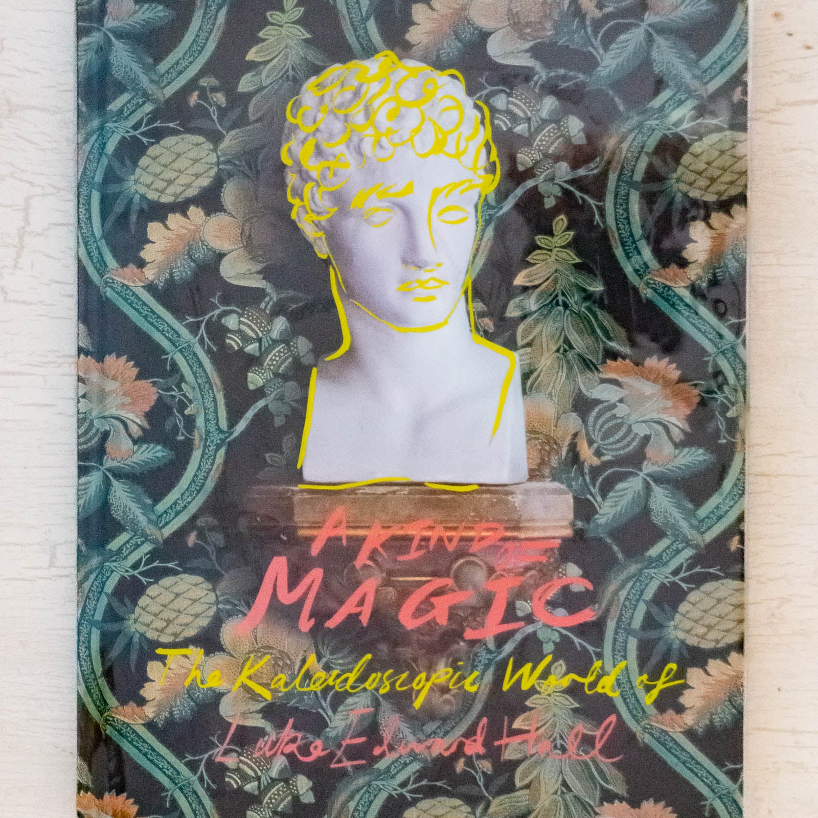 The front cover of A Kind of Magic by Luke Edward Hall. A floral background with the head of a statue, overlaid with yellow doodles.