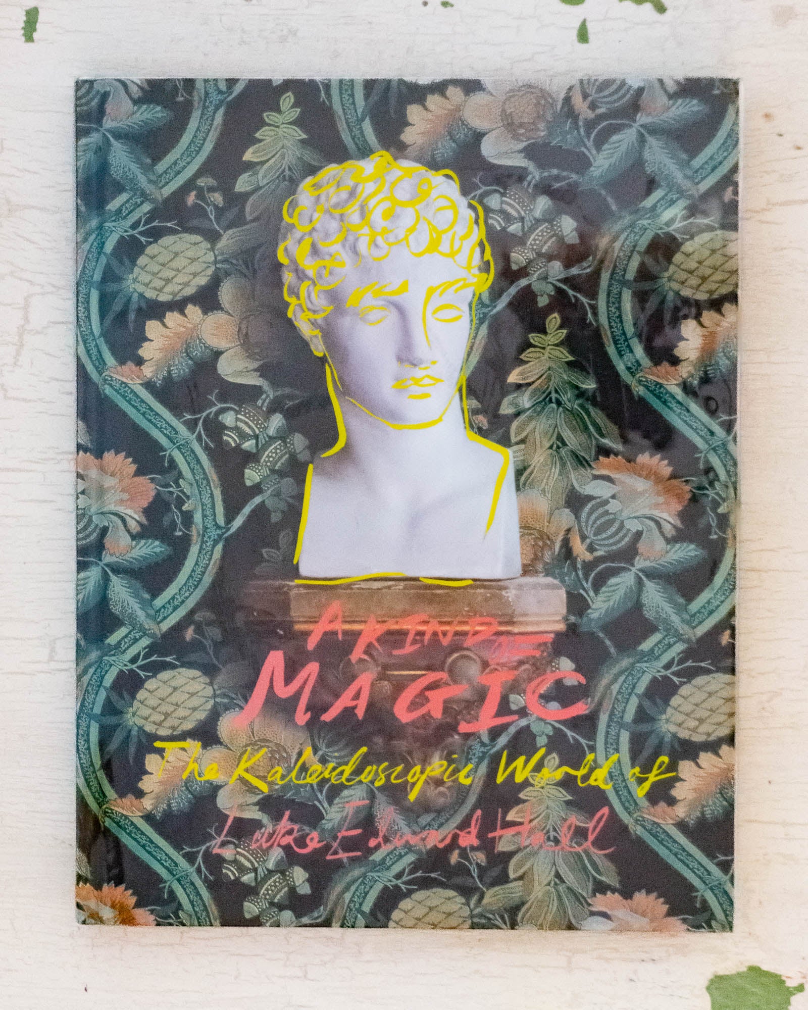The front cover of A Kind of Magic by Luke Edward Hall. A floral background with the head of a statue, overlaid with yellow doodles.