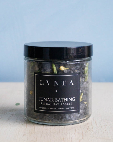 Clear glass jar filled with dark coloured coarse bath salts, dried lavender and jasmine flowers and dried oat tops by Lvnea.