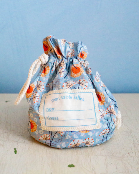A blue and orange cloth bag of Moulin Roti marbles with a drawstring and a spot for writing a child's name