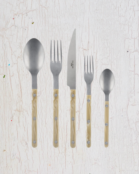 Set of stainless steel cutlery with beige acrylic handles: from left to right, a soup spoon, a dinner fork, a knife, a desert fork and teaspoon. By Sabre Paris.